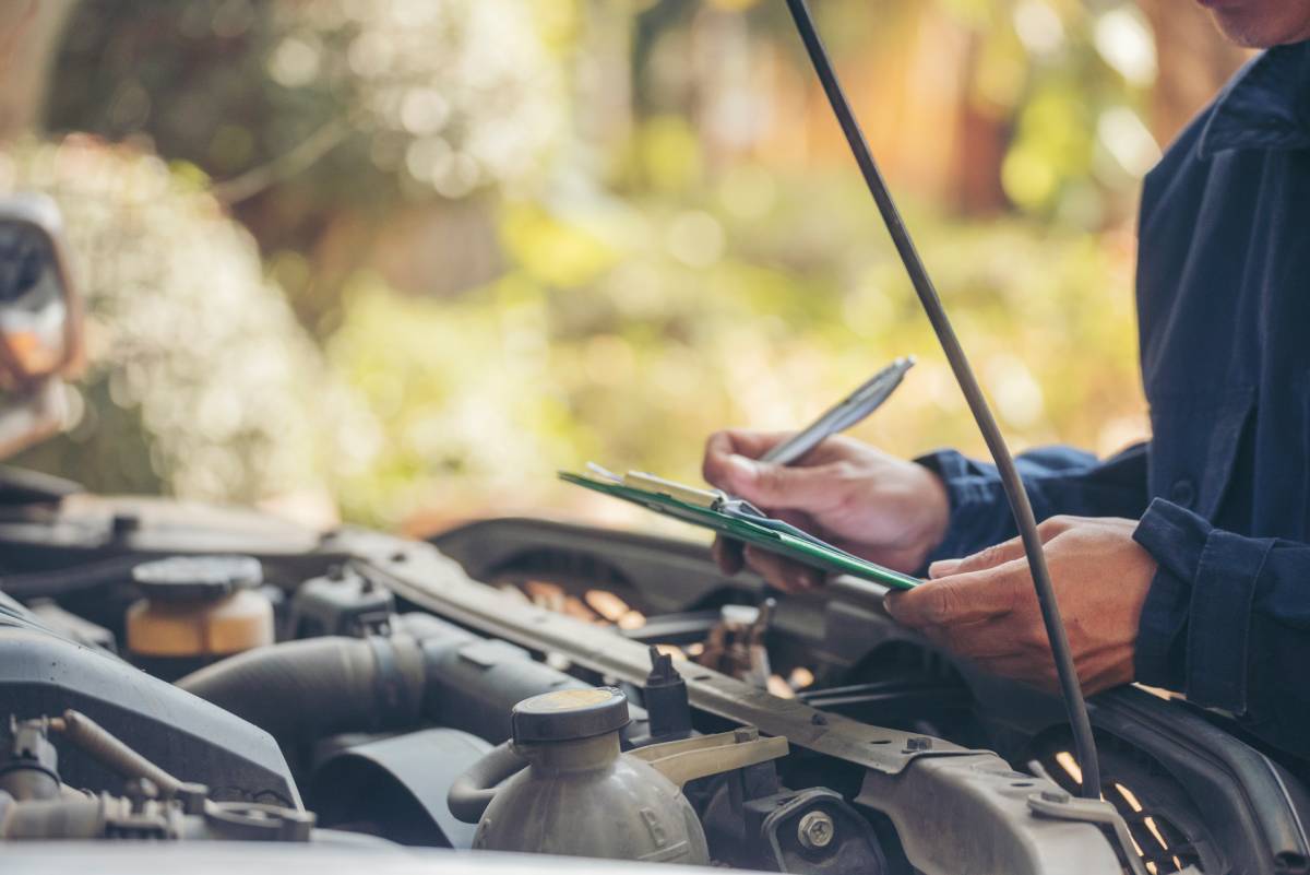 A mechanic standing over an engine with a clipboard and pen